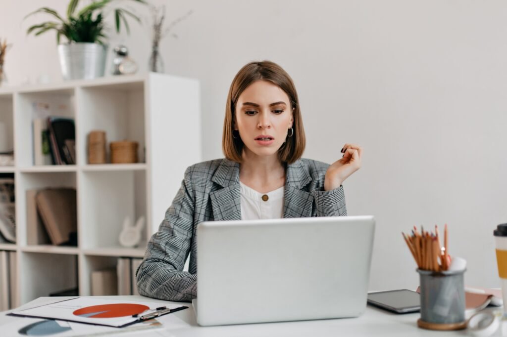 Serious business woman with anxiety looks in Macbook. Portrait of girl with short haircut in white