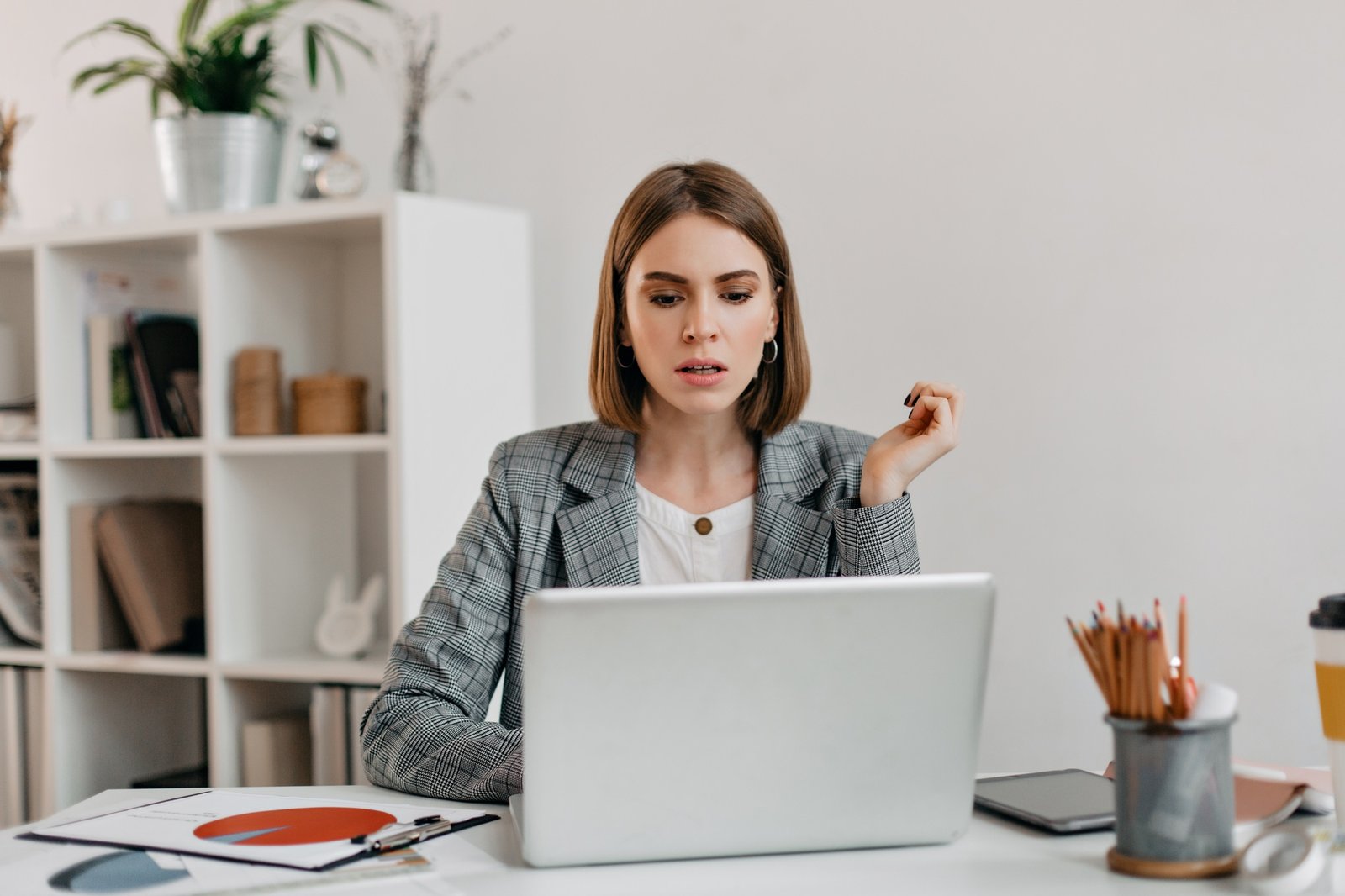 Serious business woman with anxiety looks in Macbook. Portrait of girl with short haircut in white